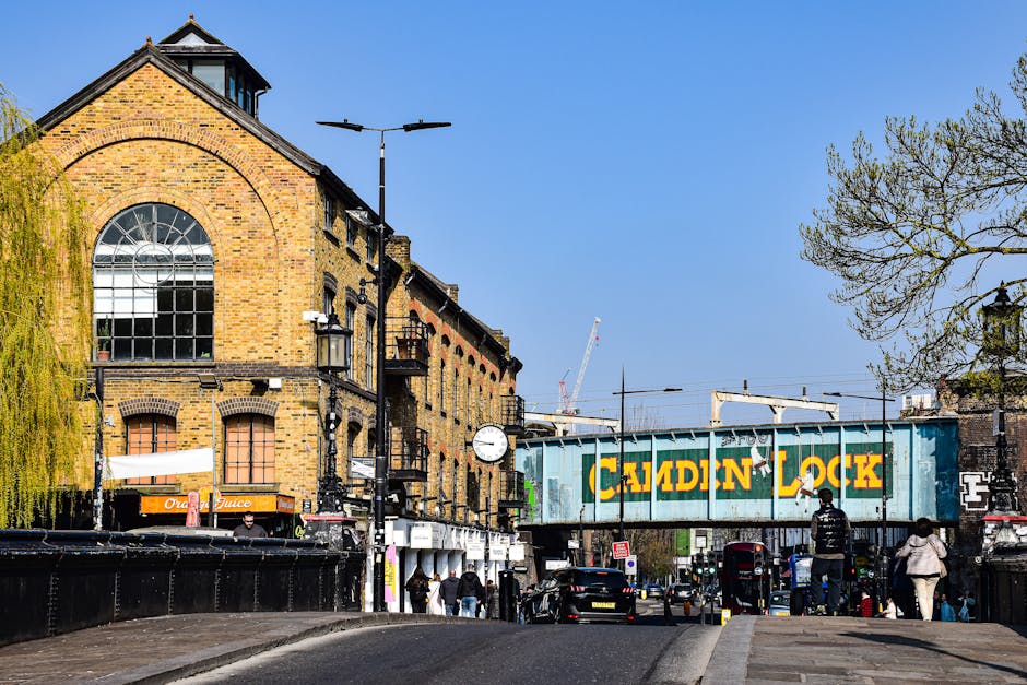 A busy street scene in Clapham with a historic white church tower featuring a gold weather vane visible in the background, surrounded by a mix of Georgian and Victorian-style buildings with shopfronts